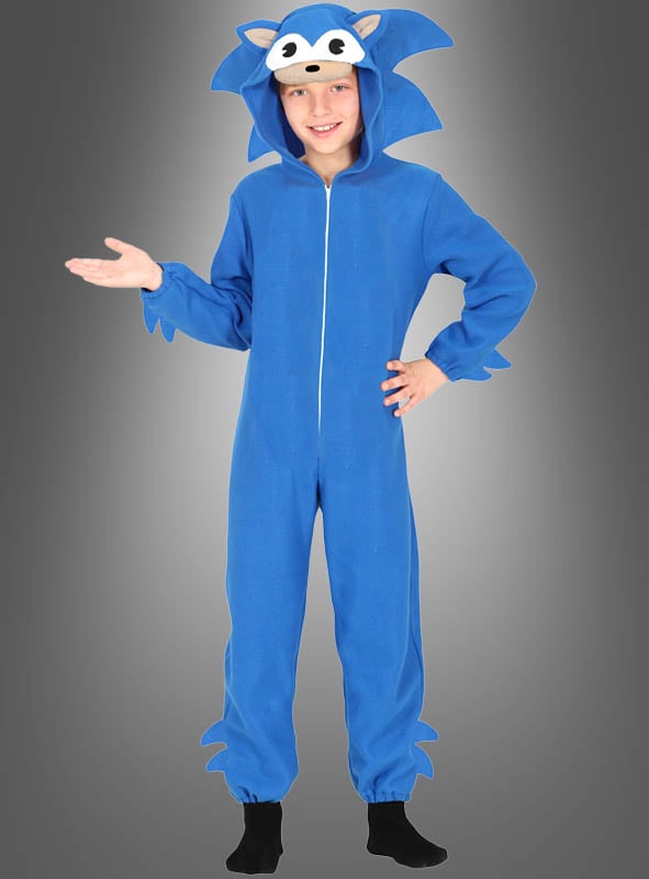 Ein Kind, das einen blauen Kigurumi-Igel-Overall für Kinder trägt, steht lächelnd mit einer erhobenen Hand vor einem einfarbigen Hintergrund mit Farbverlauf.