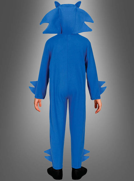 Eine Person trägt den Kigurumi „Igel Overall Kinder blau“ mit Stacheln an Kopf, Armen und Beinen und steht mit dem Rücken zur Kamera vor einem grauen Hintergrund mit Farbverlauf.