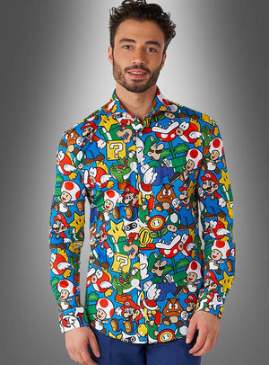 Ein Mann, der das „Super Mario Hemd“ von OppoSuits trägt – ein farbenfrohes Hemd mit Knöpfen, das mit Super-Mario-Figuren und -Symbolen bedruckt ist –, steht vor einem grauen Hintergrund mit Farbverlauf.