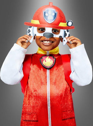 Ein lächelndes Kind, das ein rotes Marshall-Kostüm aus der „Paw Patrol Deluxe“-Reihe trägt und eine Maske mit Hundeohren und Punkten vor dem Gesicht hält – genau wie die beliebte Figur aus „Paw Patrol“.