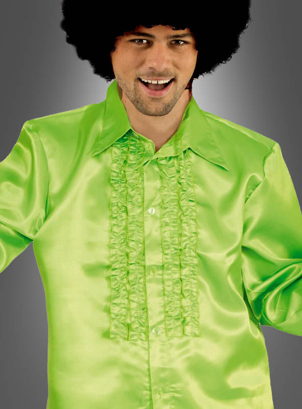 Ein Mann in einem hellgrünen, gerüschten Satinhemd im Stil der 70er Jahre mit großem Kragen und einer Afro-Perücke lächelt vor einem grauen Hintergrund – ein ideales Disco-Outfit für Herren, das den klassischen Rüschenhemd-Stil perfekt zur Geltung bringt.