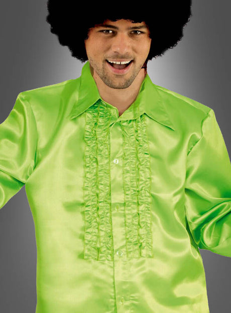 Ein Mann in einem hellgrünen, gerüschten Satinhemd im Stil der 70er Jahre mit großem Kragen und einer Afro-Perücke lächelt vor einem grauen Hintergrund – ein ideales Disco-Outfit für Herren, das den klassischen Rüschenhemd-Stil perfekt zur Geltung bringt.