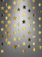 Goldene Sterne aus Papier oder Folie hängen vertikal in Reihen vor einem grauen Hintergrund mit Farbverlauf und sorgen so für einen dekorativen, festlichen Effekt – perfekt als Highlight für die Partydekoration. Die wunderschöne „Sterne-Girlande Gold“ besticht durch schimmernde Akzente aus Spiegelfolie, die jede Feier zum Strahlen bringen.