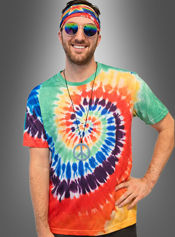 Ein Mann, der ein buntes Tie-Dye-Hemd aus dem Hippie-Kostüm-Set „Batik“ trägt und mit einem Stirnband, einer runden Sonnenbrille sowie einer Halskette mit Peace-Zeichen ausgestattet ist, steht vor einem grauen Hintergrund.