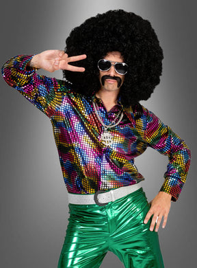 Eine Person, die ein leuchtendes „Disco Fever Rainbow Glitter“-Hemd, eine grün-metallische Hose, eine übergroße Afro-Perücke, eine Sonnenbrille und einen falschen Schnurrbart trägt, posiert vor einem grauen Hintergrund mit dem Peace-Zeichen – perfekt für ein authentisches 70er-Jahre-Kostüm.