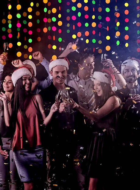 Eine Gruppe von Menschen mit Weihnachtsmützen feiert mit Getränken und Konfetti vor bunten Lichtern, umgeben von den auffälligen 80er-Jahre-Neon-Girlanden (440 cm), die einen lebhaften Schimmer verbreiten – perfekt für jede Schwarzlichtparty-Dekoration.