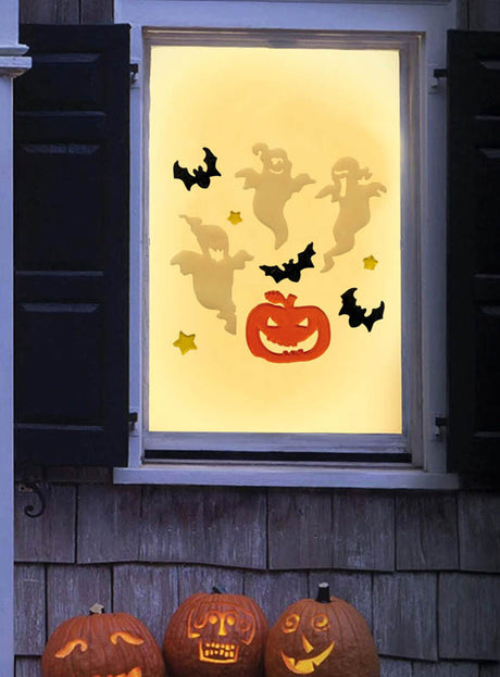 Ein Fenster ist mit Ausschnitten von Geistern, Fledermäusen, Sternen und einer Kürbislaterne verziert, die mit dem Halloween-Fenster-Deko-Set aus Gel (20 x 19 cm) gestaltet wurden. Draußen stehen drei geschnitzte Kürbisse auf der Fensterbank.