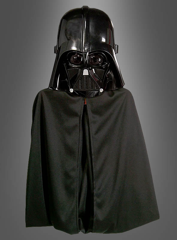 Eine Person, die den „Darth Vader Umhang mit Maske“ trägt, der der ikonischen Figur aus der „Star Wars“-Reihe sehr ähnlich sieht, steht vor einem schlichten grauen Hintergrund.