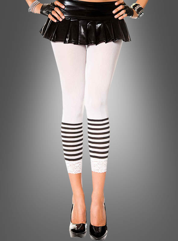Sie trägt einen schwarzen Minirock, Capri-Leggings mit Streifen aus weißem Stoff mit schwarzen Streifen und Spitzenbesatz, dazu schwarze High Heels, fingerlose Handschuhe und Armbänder, und steht vor einem grauen Hintergrund.