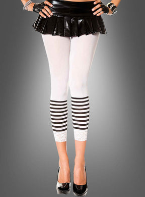 Sie trägt einen schwarzen Minirock, Capri-Leggings mit Streifen aus weißem Stoff mit schwarzen Streifen und Spitzenbesatz, dazu schwarze High Heels, fingerlose Handschuhe und Armbänder, und steht vor einem grauen Hintergrund.