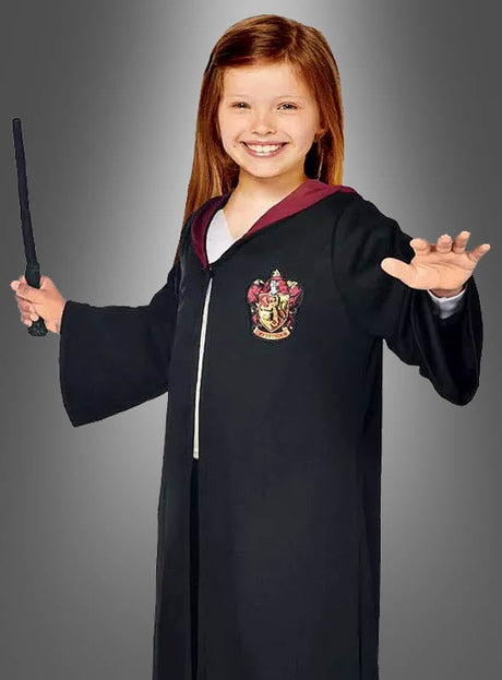 Ein junges Mädchen, das die Hermine-Granger-Gryffindor-Robe aus „Harry Potter“ mit Wappen trägt, in der einen Hand einen Zauberstab hält und die andere Hand hebt, steht vor einem schlichten grauen Hintergrund – perfekt für jedes Harry-Potter-Kostüm oder Hermine-Granger-Kostüm.