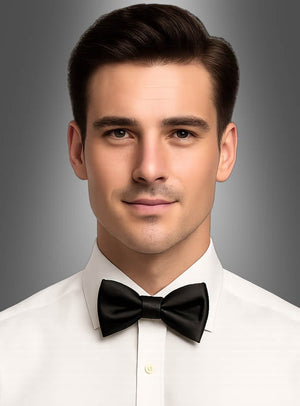 Ein Mann mit kurzen dunklen Haaren, der ein weißes Hemd und eine schwarze Satin-Fliege für Herren trägt, steht vor einem schlichten grauen Hintergrund und blickt nach vorne.