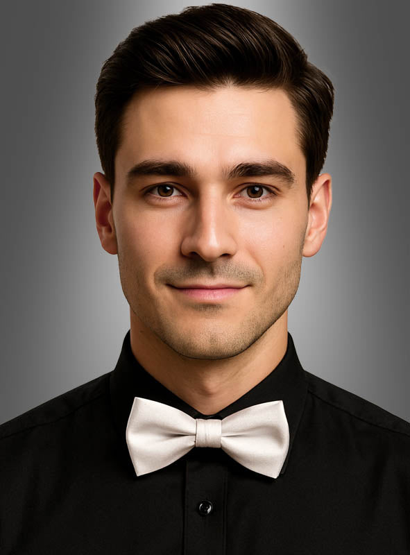 Ein Mann, der ein schwarzes Hemd und eine schwarze Satin-Fliege für Herren trägt, blickt vor einem schlichten, grau verlaufenden Hintergrund in die Kamera.