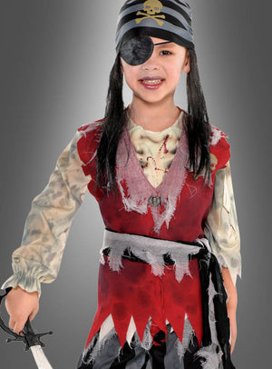 Ein Kind in einem „Toter Pirat“-Kinderkostüm – mit gestreiftem Bandana, Augenklappe, roter, zerrissener Weste und einem Spielzeugschwert in der Hand – steht vor einem grauen Hintergrund.