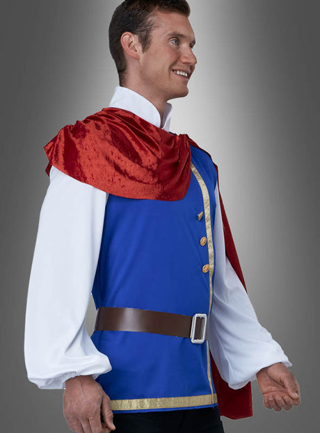 Ein Mann im „Klassischen Märchenprinz-Herrenkostüm“ – bestehend aus einer blauen Tunika mit goldenen Verzierungen, einem weißen Hemd, einem braunen Gürtel und einem roten Umhang – steht lächelnd vor einem grauen Hintergrund mit Farbverlauf; ideal für jede Märchen-Mottoparty oder als bezauberndes Märchenprinz-Karnevalskostüm.
