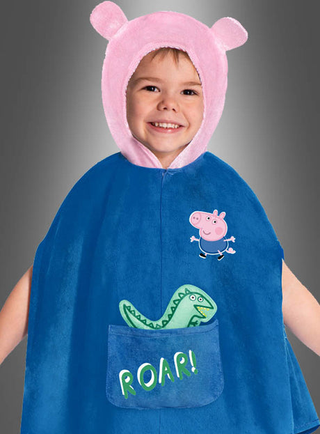 Ein lächelndes Kind, das einen blauen Umhang mit einem grünen Dinosaurier und der Aufschrift „ROAR!“ auf der Tasche sowie eine rosa Kapuze mit bärenartigen Ohren trägt, sieht in seinem George Peppa Wutz-Kostüm für Jungs bereit für ein Abenteuer aus.