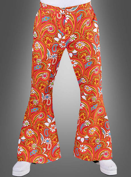 Eine Person trägt die „Bunte Schlaghose Martin für Herren“ in leuchtendem Orange mit einem auffälligen Paisley- und Blumenmuster, das an ein Kostüm aus den 70er Jahren erinnert, und steht vor einem grauen Hintergrund.
