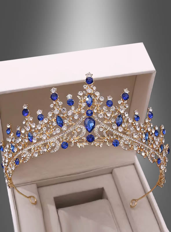 Ein „Luxus-Königinnen-Diadem mit Strass“ – eine goldene Tiara, verziert mit blauen und klaren Strasssteinen – wird in einer offenen weißen Schmuckschatulle vor grauem Hintergrund präsentiert und strahlt königliche Eleganz aus.