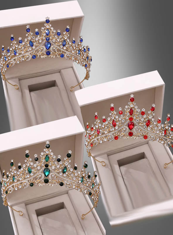Drei kunstvoll gearbeitete „Luxus Königin“-Diademe mit Strass in Gold, verziert mit blauen, grünen und roten Strasssteinen, werden in offenen weißen Schachteln vor einem grauen Hintergrund mit Farbverlauf präsentiert – jedes einzelne strahlt königliche Eleganz aus und ist die perfekte Ergänzung für jede königliche Kronensammlung.