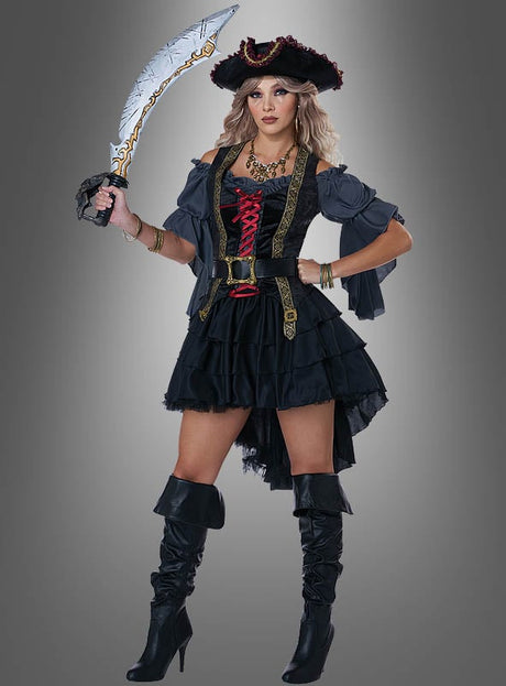 Eine Frau in einem schwarzen „Königin der Weltmeere“-Piratenkostüm mit Stiefeln und einem Piratenhut, die ein Krummschwert in der Hand hält, steht vor einem grauen Hintergrund.