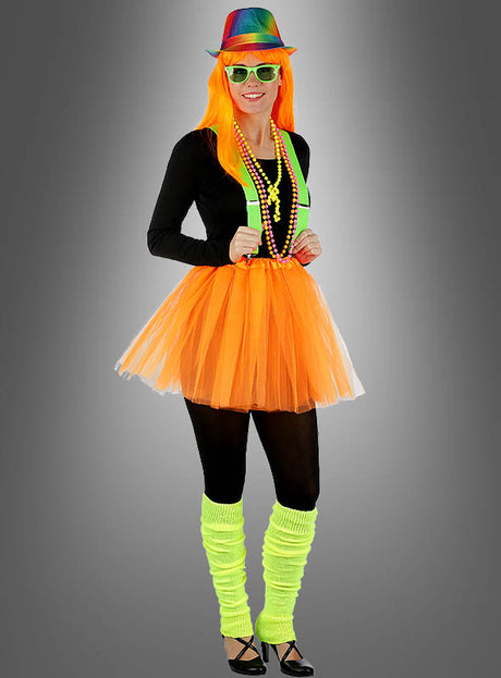 Vor einem grauen Hintergrund steht eine Person, die einen neonfarbenen Regenbogenhut, eine orangefarbene Perücke, ein schwarzes Oberteil, einen orangefarbenen Tutu-Rock, neonfarbene Hosenträger, bunte Perlen, schwarze Leggings und neongelbe Stulpen trägt – abgerundet durch eine auffällige Sonnenbrille „Party Brille“ in verschiedenen Farben. Dieser farbenfrohe Look ist das perfekte Neonparty-Accessoire für jede festliche Feier.