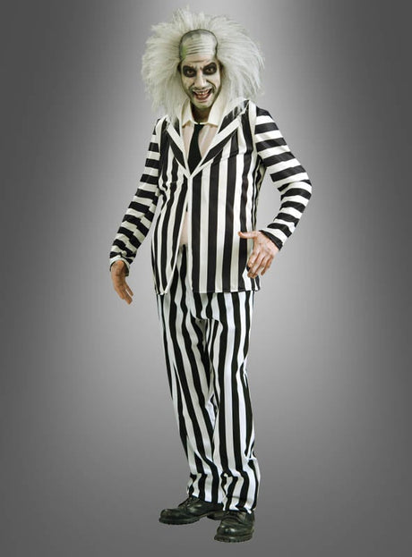 Eine Person, die das Original-Beetlejuice-Herrenkostüm trägt – bestehend aus einem schwarz-weiß gestreiften Anzug, wildem weißem Haar, blassem Make-up und schwarzen Schuhen –, steht vor einem grauen Hintergrund und verkörpert damit perfekt den kultigen Halloween-Look.