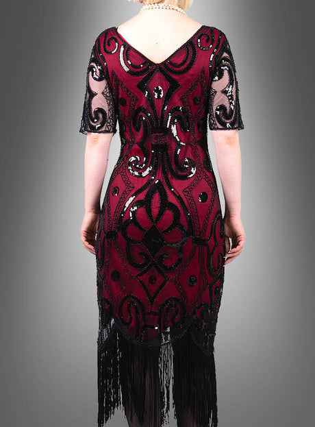 Eine Person, die das „Halbarm 20er Jahre Retro-Kleid Francis“ trägt – ein dunkelrotes Paillettenkleid mit schwarzen Mustern und Fransen – ist von hinten vor einem grauen Hintergrund zu sehen und verkörpert Vintage-Eleganz im authentischen Stil der 20er Jahre.