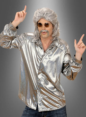 Eine Person, die ein glänzendes silbernes Disco-Hemd, eine graue Perücke, eine Sonnenbrille und einen falschen Schnurrbart trägt, posiert vor einem grauen Hintergrund, wobei beide Zeigefinger nach oben zeigen.