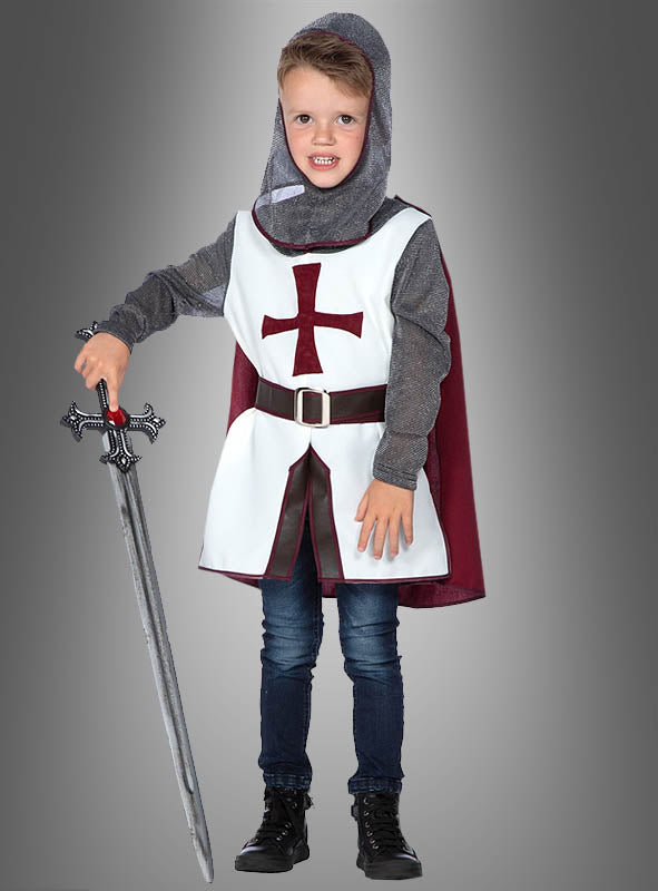 Ein kleines Kind, das das Tempelritter-Kostüm „Tristan“ für Jungen trägt – mit einem auffälligen roten Kreuz, einer grauen Kapuze und einem weinroten Umhang – und ein Spielzeugschwert in der Hand hält, steht stolz vor einem grauen Hintergrund. Dieses authentische Tempelritter-Kinderkostüm eignet sich ideal als Faschingskostüm oder für fantasievolle Rollenspiele.