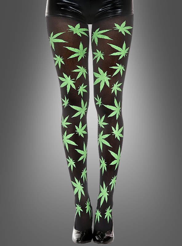 Eine Person, die die Strumpfhose „Cannabis Muster“, glänzende schwarze Shorts und schwarze High Heels trägt, steht vor einem grauen Hintergrund – ein auffälliger Look, der perfekt zu jedem Hippie-Kostüm passt.