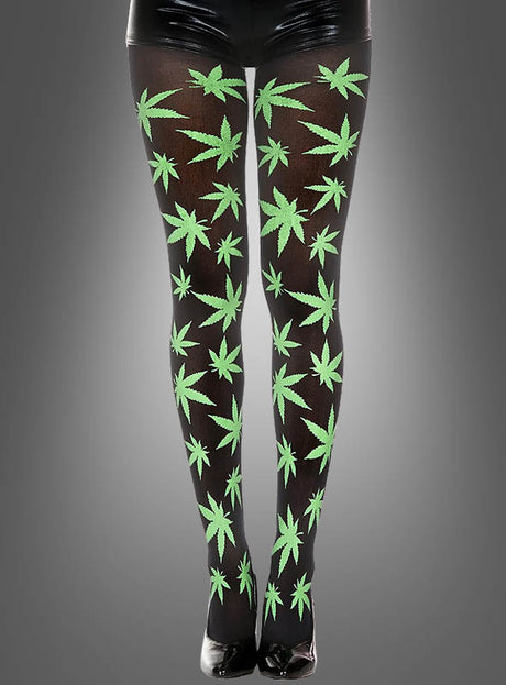 Eine Person, die die Strumpfhose „Cannabis Muster“, glänzende schwarze Shorts und schwarze High Heels trägt, steht vor einem grauen Hintergrund – ein auffälliger Look, der perfekt zu jedem Hippie-Kostüm passt.