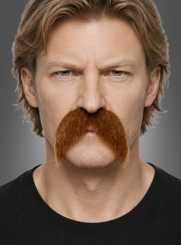 Ein Mann mit hellbraunen Haaren und ernstem Gesichtsausdruck trägt den „Großer Schnurrbart braun oder schwarz“, einen großen, buschigen Schnurrbart, der an den klassischen Schnauzer-Stil erinnert.
