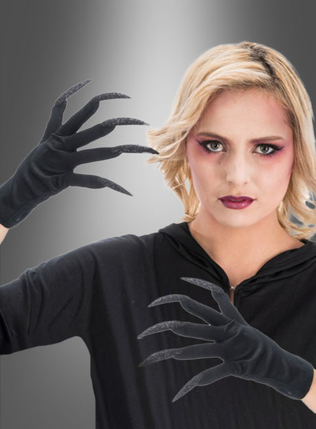 Eine Person mit blonden Haaren und auffälligem Make-up trägt schwarze Handschuhe mit Fingernägeln und ein schwarzes Oberteil und posiert mit erhobenen Händen vor einem grauen Hintergrund mit Farbverlauf – perfekt für ein auffälliges Halloween-Kostüm.