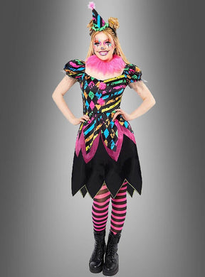 Eine Person im „Zirkus Clown Neon Kostüm Damen“ – einem farbenfrohen Harlekin-Clownkostüm mit rosa Rüschen, gestreifter Mütze, auffälligem Make-up und rosa-schwarz gestreiften Leggings – steht vor einem grauen Hintergrund – perfekt für Ihre nächste Feier.