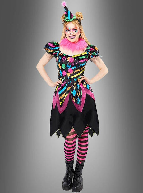Eine Person im „Zirkus Clown Neon Kostüm Damen“ – einem farbenfrohen Harlekin-Clownkostüm mit rosa Rüschen, gestreifter Mütze, auffälligem Make-up und rosa-schwarz gestreiften Leggings – steht vor einem grauen Hintergrund – perfekt für Ihre nächste Feier.