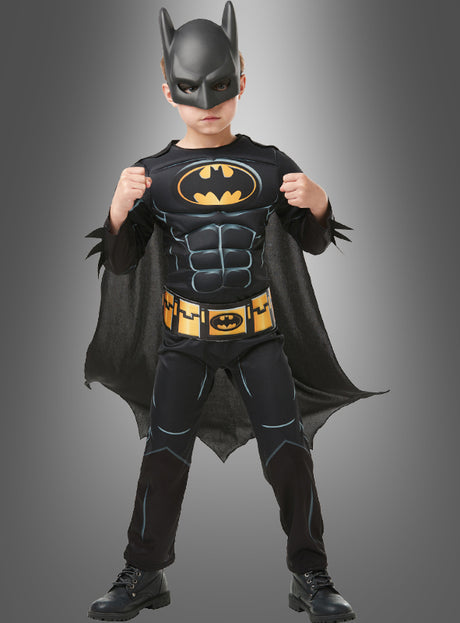 Ein Kind trägt ein Batman-Kinderkostüm mit Maske und steht mit erhobenen Fäusten nach vorne gewandt.