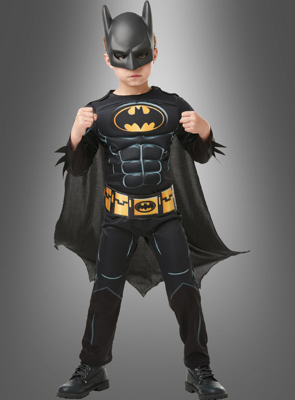 Ein Kind trägt ein Batman-Kinderkostüm mit Maske und steht mit erhobenen Fäusten nach vorne gewandt.