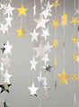Gold- und silberfarbene „Sternengirlande“-Partydeko (360–400 cm) hängt an Schnüren vor einem schlichten grauen Hintergrund und sorgt so für eine festliche Dekoration, die sich perfekt für jede Party im Hollywood-Stil eignet.