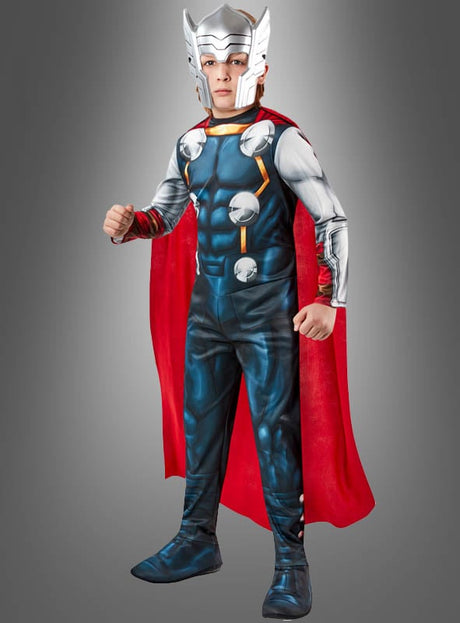 Ein Kind, das das Thor-Kinderkostüm „Superheld“ trägt – bestehend aus einem silbernen Helm, einem roten Umhang und einem blauen Anzug mit rüstungsartigen Details –, steht vor einem grauen Hintergrund.