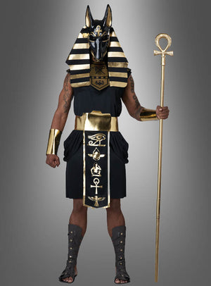 Eine Person trägt das „Ägyptischer Gott Anubis Deluxe“-Kostüm, bestehend aus einer auffälligen schwarz-goldenen Anubis-Maske, einem Kopfschmuck, einem Stab, goldenen Armreifen und Sandalen, und steht vor einem grauen Hintergrund als Gott der Toten.