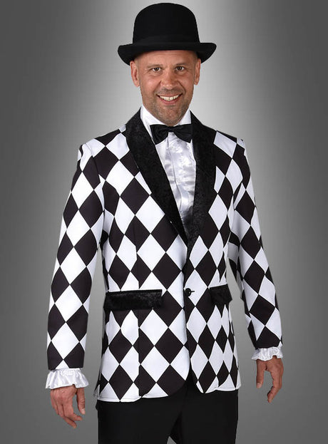 Ein Mann steht lächelnd vor einem schlichten grauen Hintergrund und trägt das „Sakko mit Schachbrettmuster schwarz-weiß“ sowie ein weißes Hemd, eine schwarze Fliege und einen schwarzen Bowlerhut.
