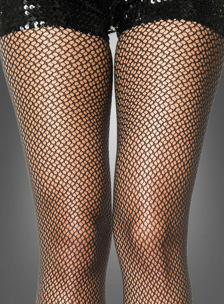 Nahaufnahme der Beine einer Person, die eine elegante schwarze Strumpfhose mit Netzmuster sowie schwarze Shorts mit Pailletten trägt, vor einem grauen Hintergrund.