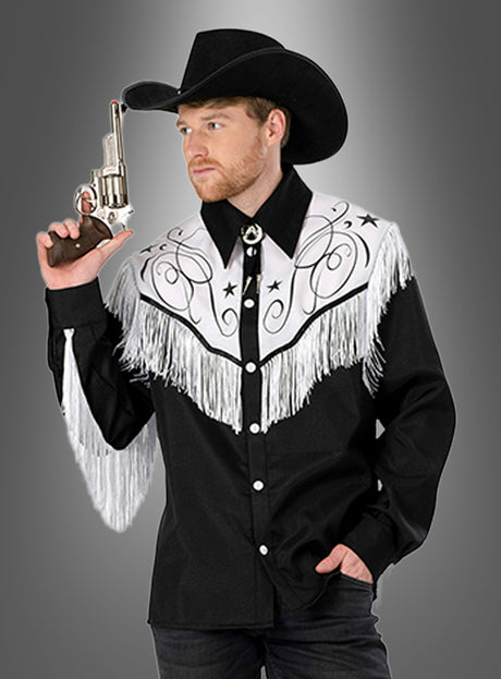 Ein Mann mit einem schwarzen Cowboyhut und einem Cowboyhemd mit Fransen hält einen Revolver in der Hand und blickt vor einem grauen Hintergrund mit Farbverlauf zur Seite.