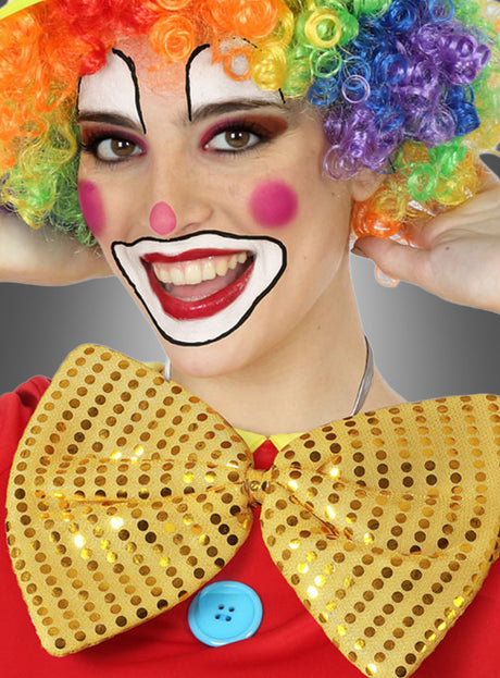 Eine als Clown verkleidete Person mit einer Regenbogenperücke, bunter Gesichtsbemalung und einem roten Hemd mit blauem Knopf lächelt in die Kamera, während sie die „Riesenfliege Karneval“ in verschiedenen Farben als große Fliege aus goldenen Pailletten trägt.