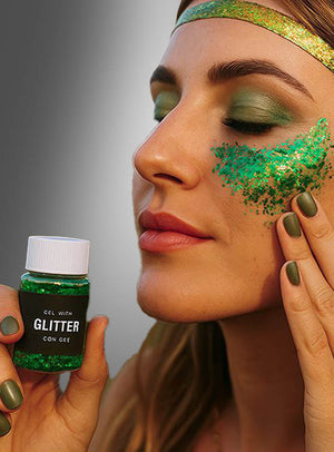 Eine Person trägt Glittergel-Make-up in verschiedenen Grüntönen auf ihre Wange auf und präsentiert so einen funkelnden Glitzer-Make-up-Look. Dazu trägt sie passenden grünen Lidschatten, grünen Nagellack und ein glänzendes grünes Stirnband.