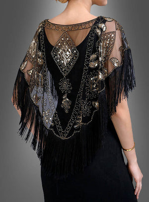 Eine Frau, die von hinten zu sehen ist, trägt ein schwarzes Kleid, dazu den „20er-Jahre-Kurzumhang mit Fransen“ – ein transparentes, mit Perlen besticktes Cape mit geometrischen und floralen Mustern, das an den Stil der 1920er Jahre erinnert.