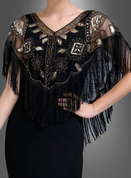 Eine Person trägt den „20er Jahre Kurzumhang mit Fransen“ – ein schwarzes Überkleid aus transparentem Stoff mit perlenbesetzten Fransen sowie geometrischen und blattförmigen Mustern in Gold und Silber – ein elegantes Accessoire, das perfekt zu einem Charleston-Kleid passt.