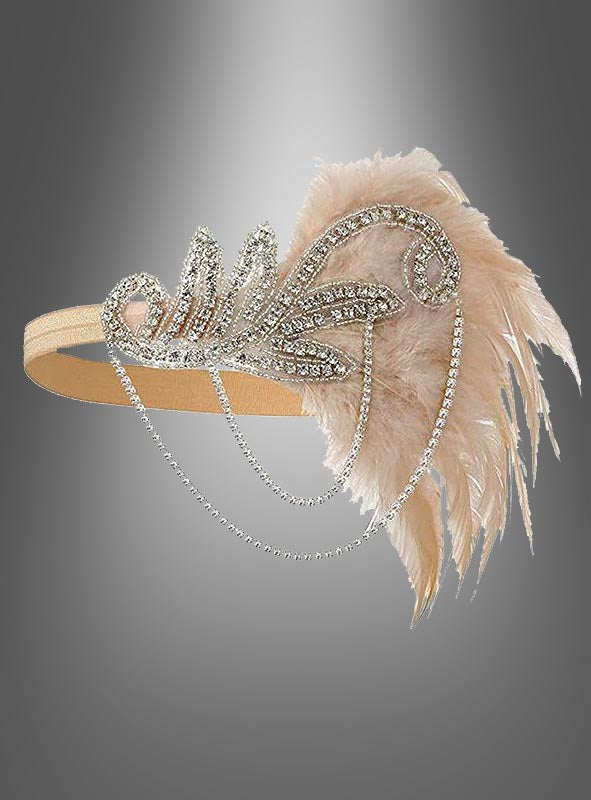Der Kopfschmuck „20er Jahre mit Strass Alice“ ist ein beiges Haarband, das mit Strasssteinen und Perlen verziert ist und zarte, blassrosa Federn sowie herabhängende Perlenstränge aufweist. Es erinnert an den Glamour des Vintage-Kopfschmucks der 20er Jahre und lässt sich mühelos mit jedem Charleston-Kleid kombinieren. Vor einem grau verlaufenden Hintergrund präsentiert, verkörpert dieses elegante Haarband die Essenz zeitloser Raffinesse.