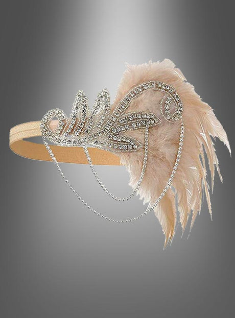 Der Kopfschmuck „20er Jahre mit Strass Alice“ ist ein beiges Haarband, das mit Strasssteinen und Perlen verziert ist und zarte, blassrosa Federn sowie herabhängende Perlenstränge aufweist. Es erinnert an den Glamour des Vintage-Kopfschmucks der 20er Jahre und lässt sich mühelos mit jedem Charleston-Kleid kombinieren. Vor einem grau verlaufenden Hintergrund präsentiert, verkörpert dieses elegante Haarband die Essenz zeitloser Raffinesse.