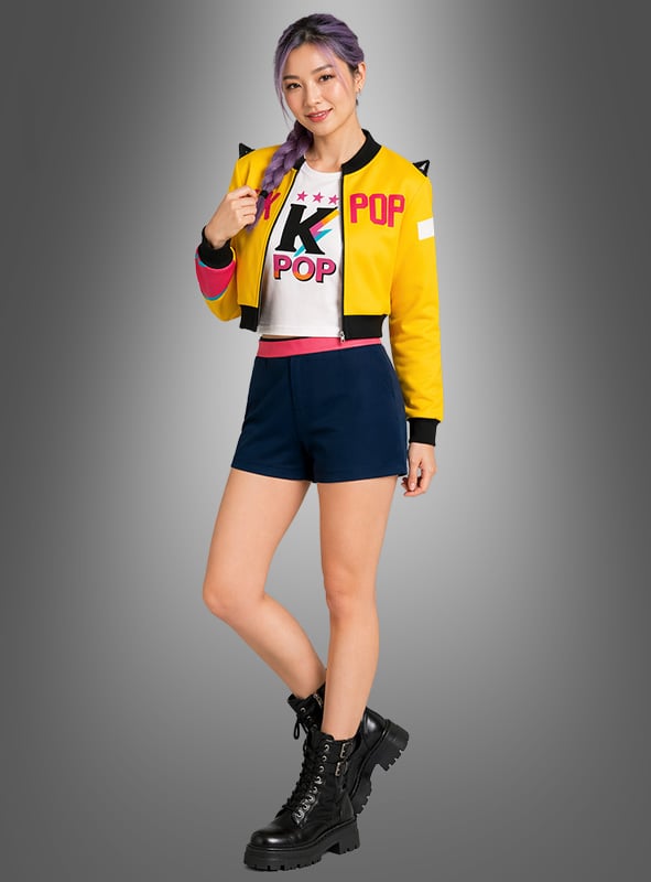 Eine Frau mit lila Haaren trägt das K-Pop-Romy-Outfit für Damen mit Jacke – eine gelbe Jacke, ein weißes K-Pop-Shirt, marineblaue Shorts und schwarze Stiefel –, während sie vor einem grauen Hintergrund mit Farbverlauf steht.